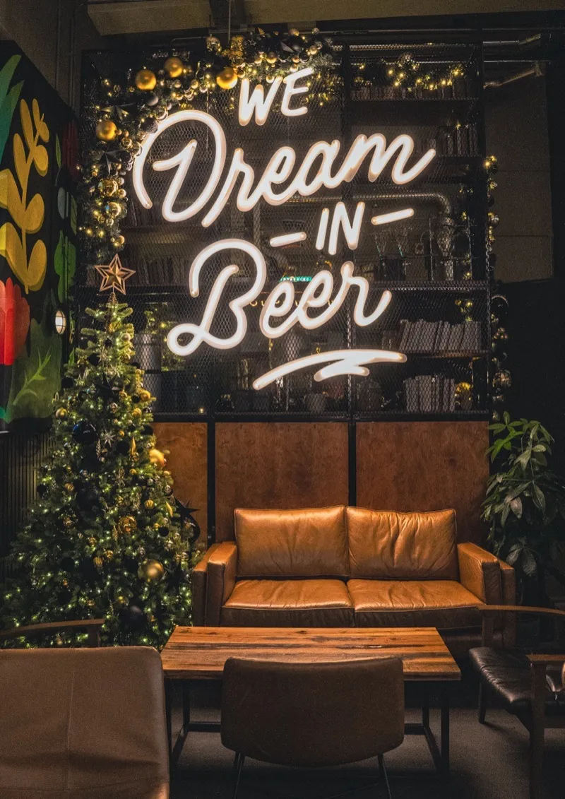 Neon sign reading We Dream in Beer with leather seating and Christmas tree