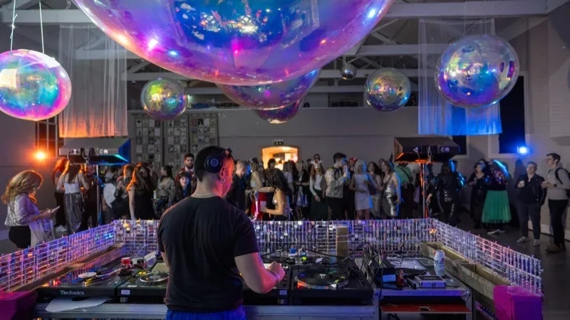 DJ behind the decks with crowd and iridescent balloons at Richmond Barracks